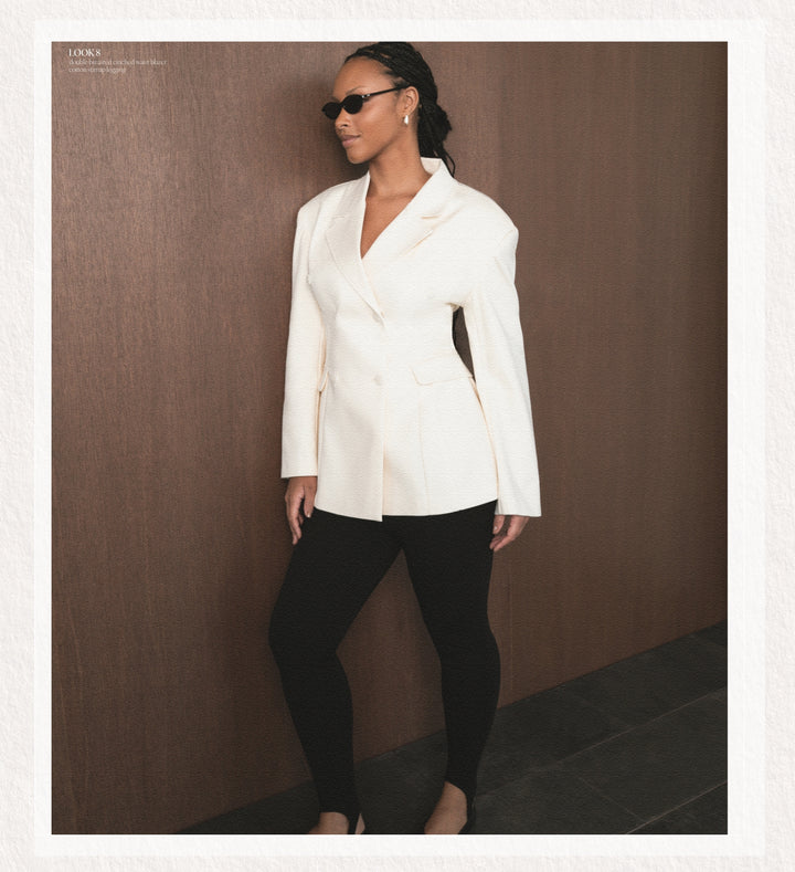 Woman wearing a white blazer and black pants against a brown background