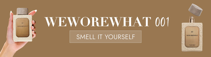Perfume bottle held by a hand with 'WEWOREWHAT 001' text on a brown background
